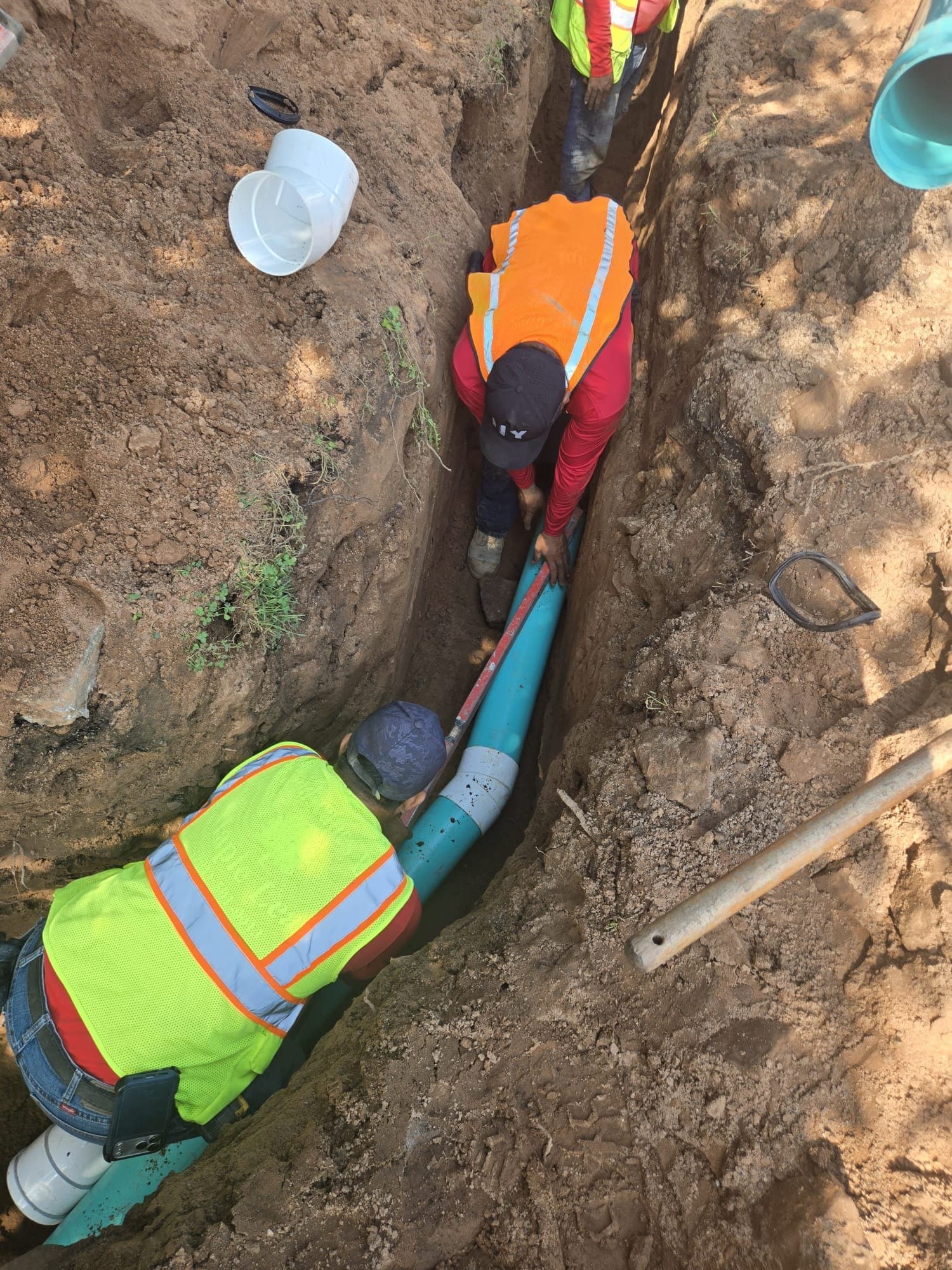 Two crew members in a narrow trench joining solid drain pipe below a lawn