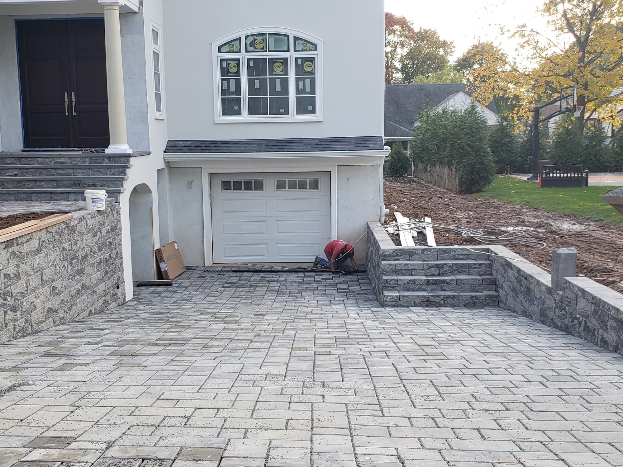 Wide paver driveway running up to a two-car garage between new stone curb walls