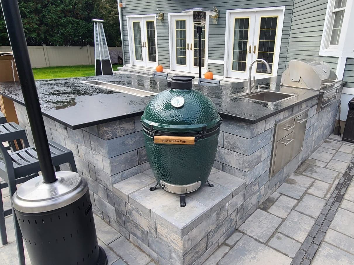Outdoor kitchen island with a kamado grill and a bar counter running back to the house