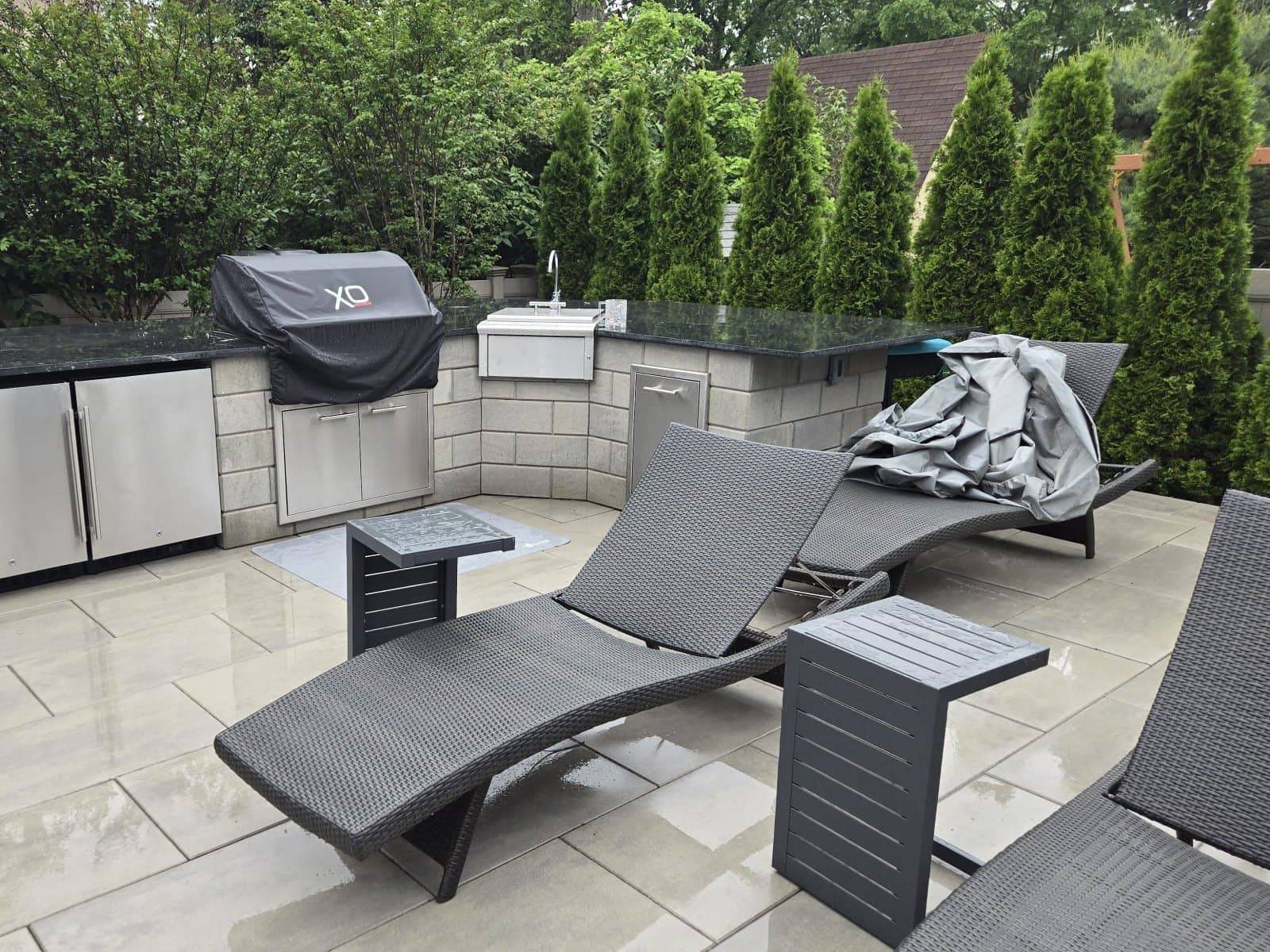 Stone outdoor kitchen with a built-in grill and sink behind loungers on a paver patio