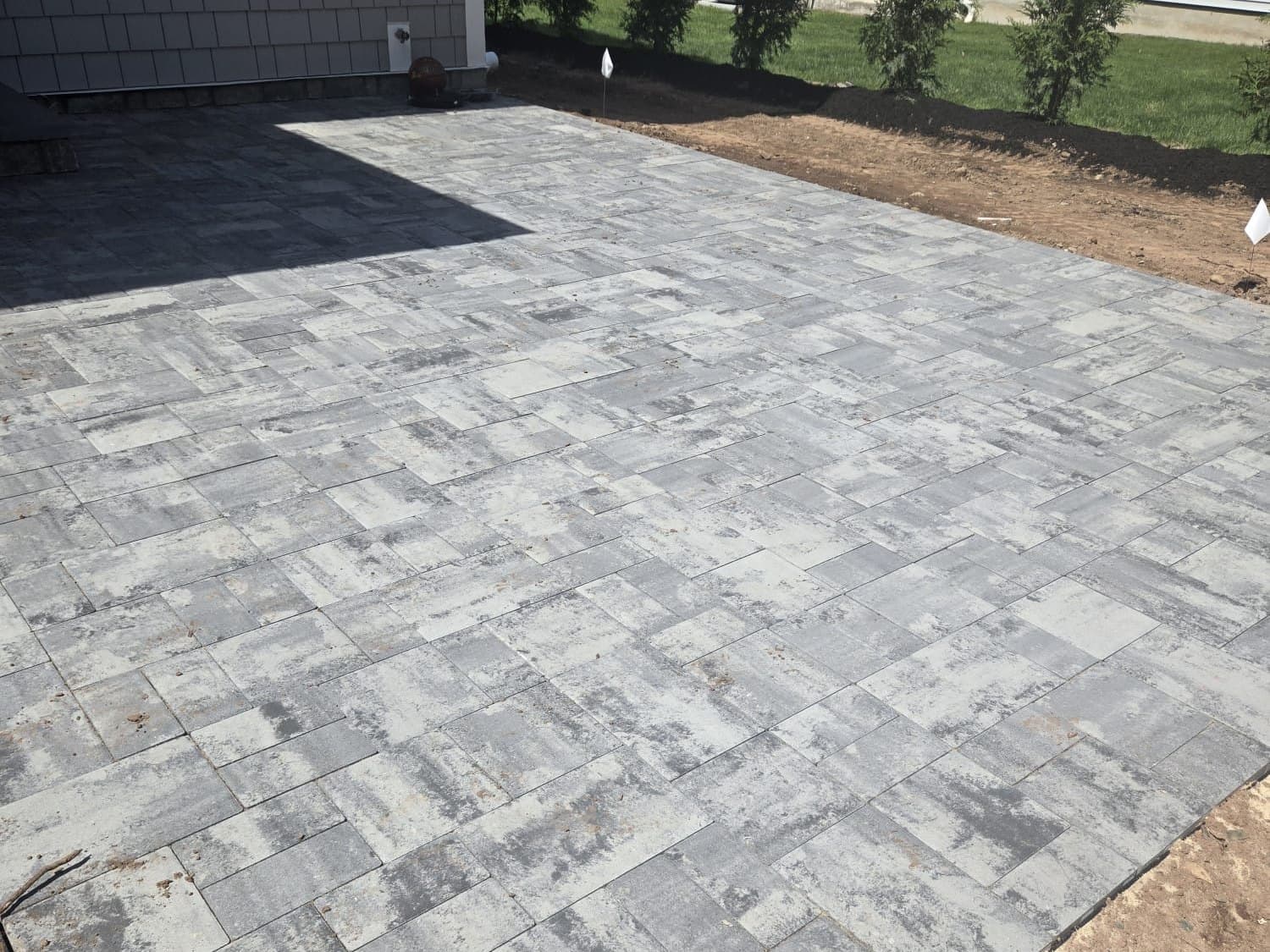 Large-format paver patio wrapping the side of a house, edged against a new lawn