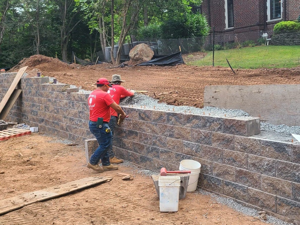 Two masons setting block on a new retaining wall, with drainage stone backfilled behind it